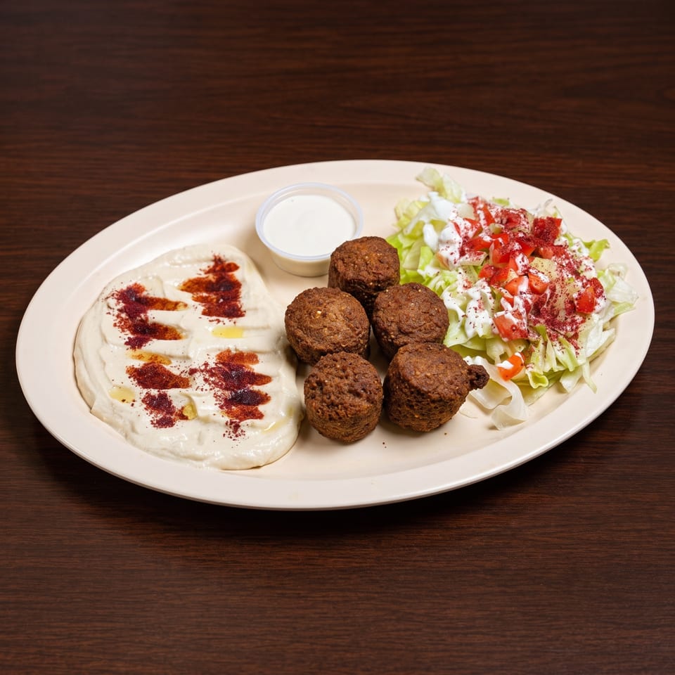 A plate of falafel, hummus with paprika and olive oil, a side salad, and white sauce.