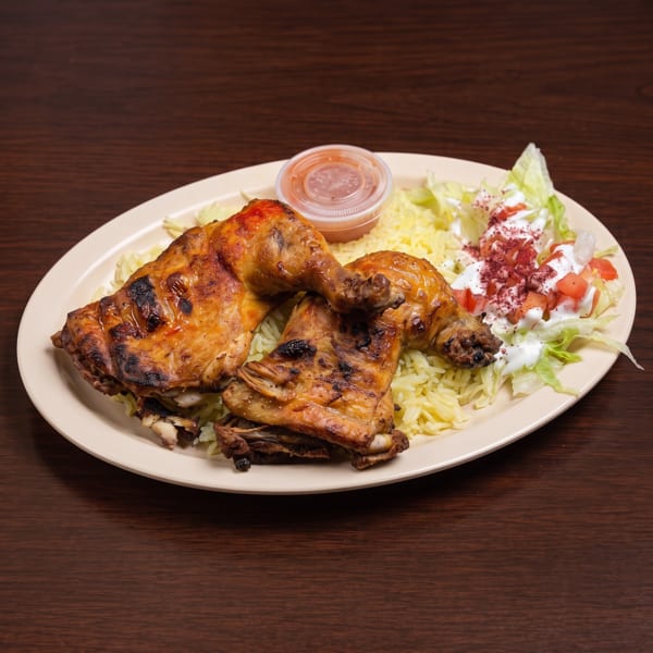 Grilled chicken legs with yellow rice, a side salad, and a small cup of sauce on a white plate.