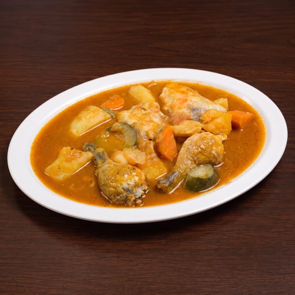 Chicken stew with vegetables like carrots, potatoes, and zucchini in a rich orange broth.