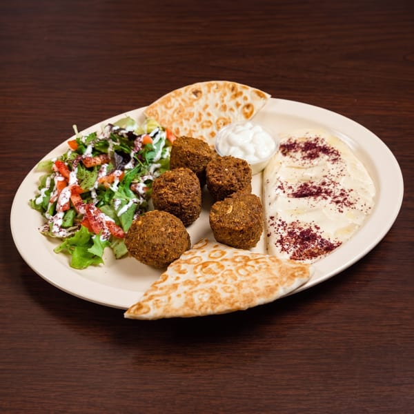 Falafel platter with hummus, salad, pita bread, and white sauce on a wooden table.