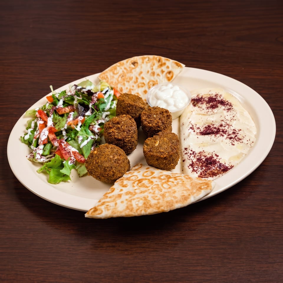 Falafel platter with hummus, salad, pita bread, and white sauce on a wooden table.