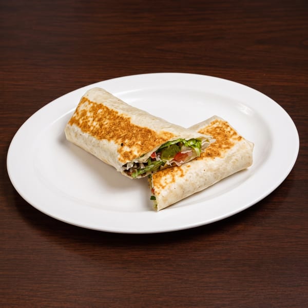Two halves of a grilled burrito, filled with lettuce, tomatoes, and meat, on a white plate.