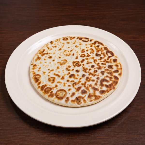A round, lightly browned flatbread on a white plate, centered on a dark wooden table.