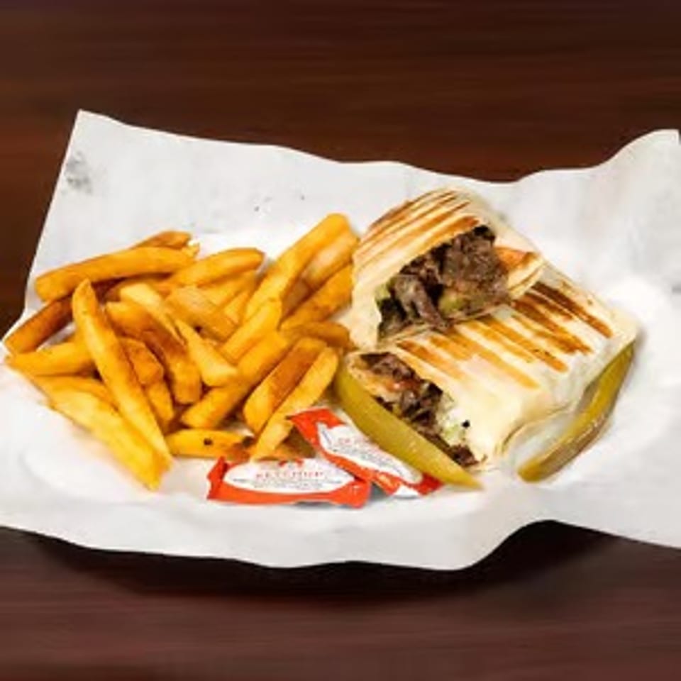 Grilled shawarma wrap cut in half, served with golden french fries and pickles on white paper.