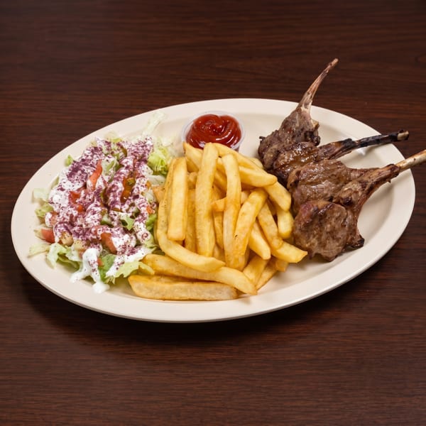 Grilled lamb chops with french fries, a side salad, and a small cup of ketchup on a white plate.