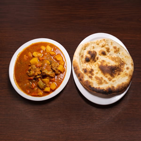 Chicken curry with potatoes and carrots in a white bowl, next to a round naan bread.