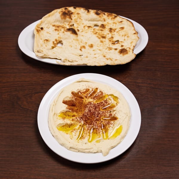 A plate of hummus drizzled with olive oil and spices, with a plate of flatbread above it.