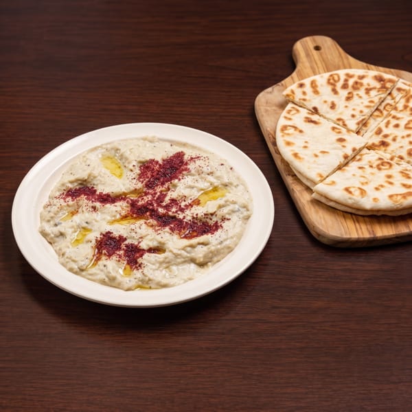 Baba Ghanoush with olive oil and sumac, served with pita bread on a wooden board.