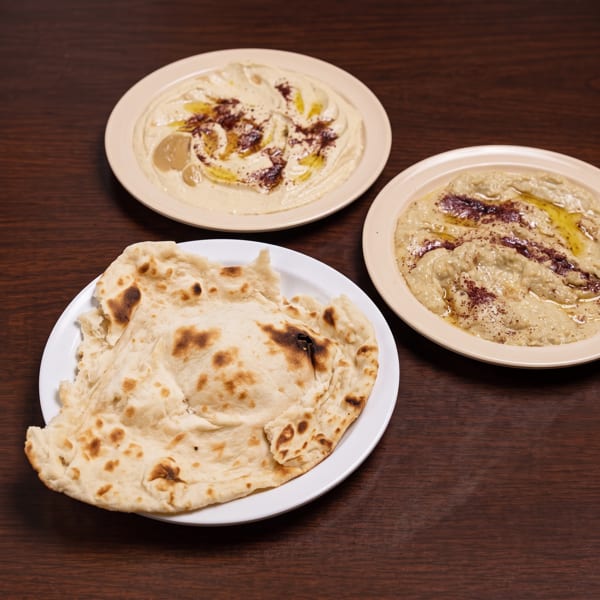 Two plates of hummus and baba ghanoush with a side of fresh pita bread.