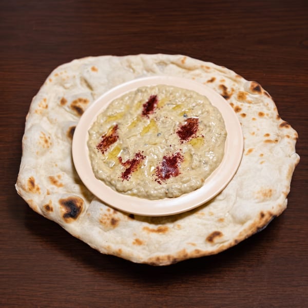 A plate of baba ghanoush with olive oil and sumac, served on a large flatbread.