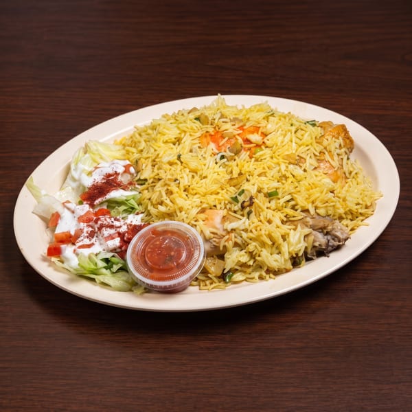 A plate of yellow rice with chicken, a side salad with dressing, and a small cup of red sauce.